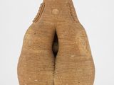 une petite figurine en argile représentant une femme, les mains dans les poches