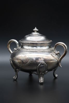 une théière ancienne en argent posée sur un support, sur fond noir
