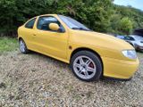 a picture of a yellow car parked in a gravel lot
