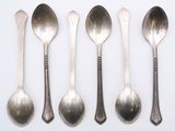six spoons and a spoon rest on a white surface