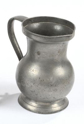un pichet en argent posé sur une surface blanche, à côté d'une tasse