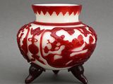a red and white vase on a stand on a gray surface