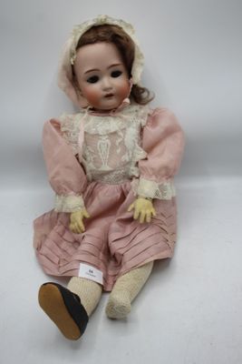 une poupée ancienne assise sur une surface blanche, vêtue d'une robe rose et d'un bonnet