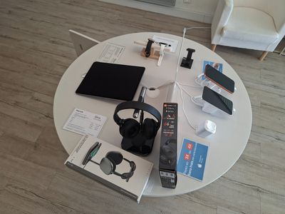 une table sur laquelle se trouvent un ordinateur portable, un casque, une télécommande et d'autres appareils électroniques