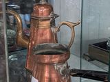 a glass case with a copper coffee pot on top of it
