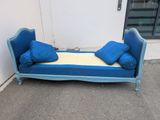 a blue day bed with pillows on it in front of a white wall