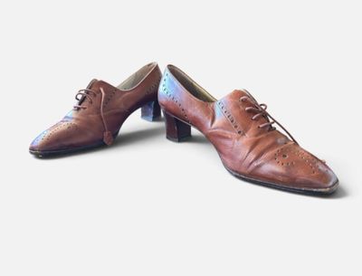 une paire de chaussures en cuir marron à lacets posée sur une surface blanche