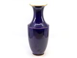 un vase bleu à bord doré posé sur une surface blanche