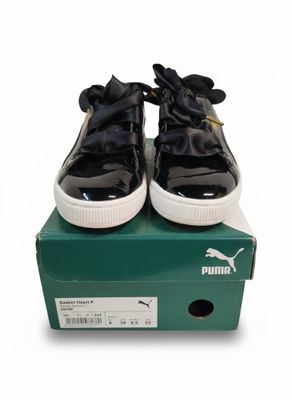 des baskets Puma noires et blanches ornées de nœuds, posées sur une boîte verte