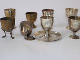 cinq gobelets en argent et une coupe en argent posés sur une table blanche