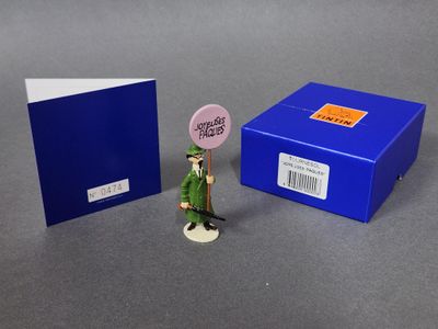 une petite figurine représentant un homme en costume vert, à côté d'une boîte bleue