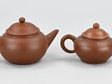 two brown ceramic teapots with lids sit on a white surface