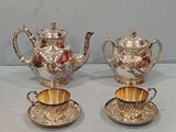 three silver teapots and a cup on a table