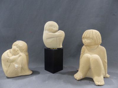 trois sculptures en céramique représentant des enfants assis sur un socle, dont l'un tient un bébé dans ses bras
