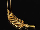 a gold plated brooch with a feather on top of it