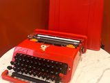 a red typewriter sitting on a table next to a red book