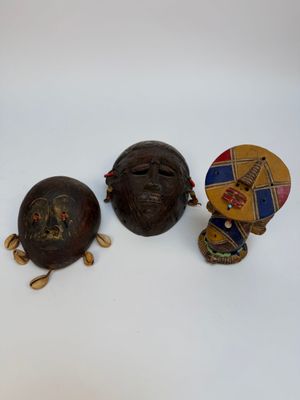 trois masques africains sont posés les uns à côté des autres sur une surface blanche
