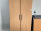 a tall wooden cabinet next to a black trash can