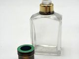 a small glass bottle with a green lid next to a small glass container