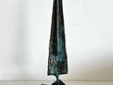 sculpture en bronze représentant un cône posé sur un socle, sur une surface blanche