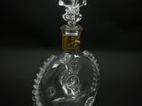 une bouteille en verre transparent avec un bouchon doré, posée sur une surface noire