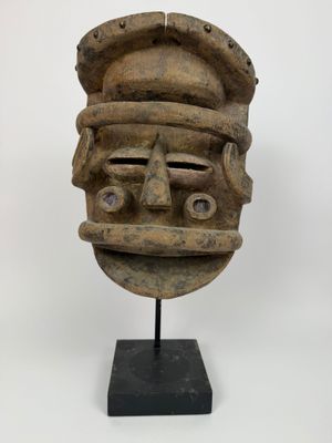 un masque en bois posé sur un socle noir, sur fond blanc