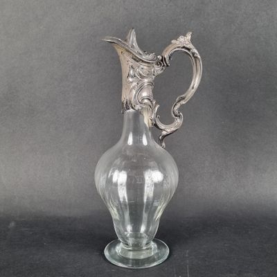 un vase en verre muni d'une poignée en argent, posé sur une table