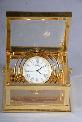 une horloge en or posée dans une vitrine, sur un support blanc