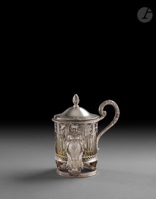 une théière ancienne en argent, avec un couvercle et une anse, posée sur un support gris