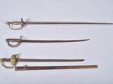 three old swords are displayed in a row on a white surface