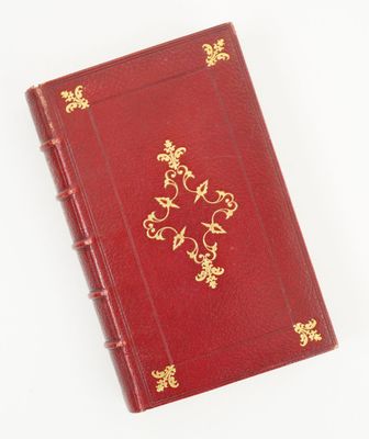 un vieux livre rouge avec des bordures dorées posé sur une surface blanche