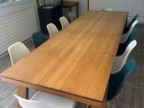 une grande table en bois avec des chaises blanches et un tableau accroché au mur