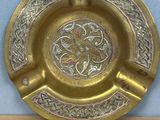 brass ashtray with celtic design on top of a wooden table