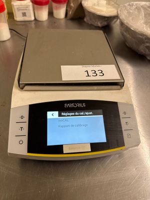 une balance numérique posée sur une table, avec de nombreux ingrédients en arrière-plan