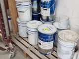 several buckets of paint are stacked on a pallet in a garage