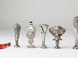 five silver vases and a red flower on a white surface