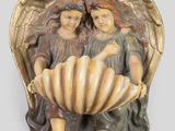 figurine d'ange tenant un coquillage sur lequel sont assis deux enfants