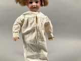 an old fashioned doll with brown hair and a white dress