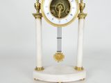 une horloge blanche et dorée posée sur un socle, avec une paire de ciseaux à côté