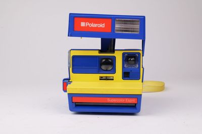 un appareil photo Polaroid jaune et bleu posé sur une surface blanche