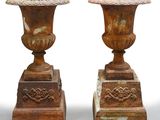 une paire d'urnes anciennes en fonte posées sur des socles, sur fond blanc