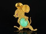 a close up of a gold mouse broochle with a green stone