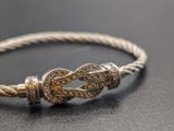 silver and gold bracelet with a knot on it on a black surface