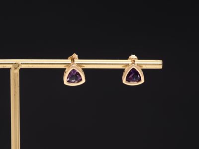a pair of gold earrings with amethtites on a black background