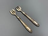 deux fourchettes et un couteau posés sur une table, sur fond gris