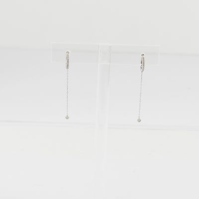 une paire de boucles d'oreilles en argent posée sur un socle en acrylique transparent, sur une surface blanche