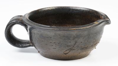 une tasse noire avec une anse posée sur une surface blanche