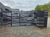 une pile de palettes en plastique noir posée sur un terrain recouvert de gravier
