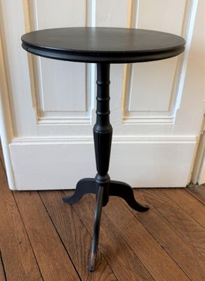 une image représentant une table noire posée sur un parquet, devant une porte
