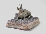 statue of a goat sitting on a rock on a white surface